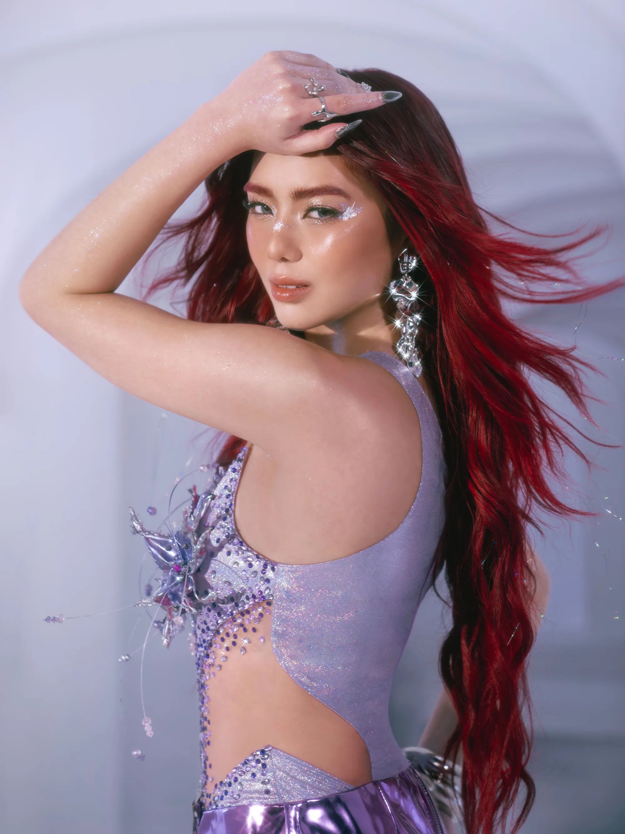 A BINI member with red hair, in profile, in a lilac sequined top