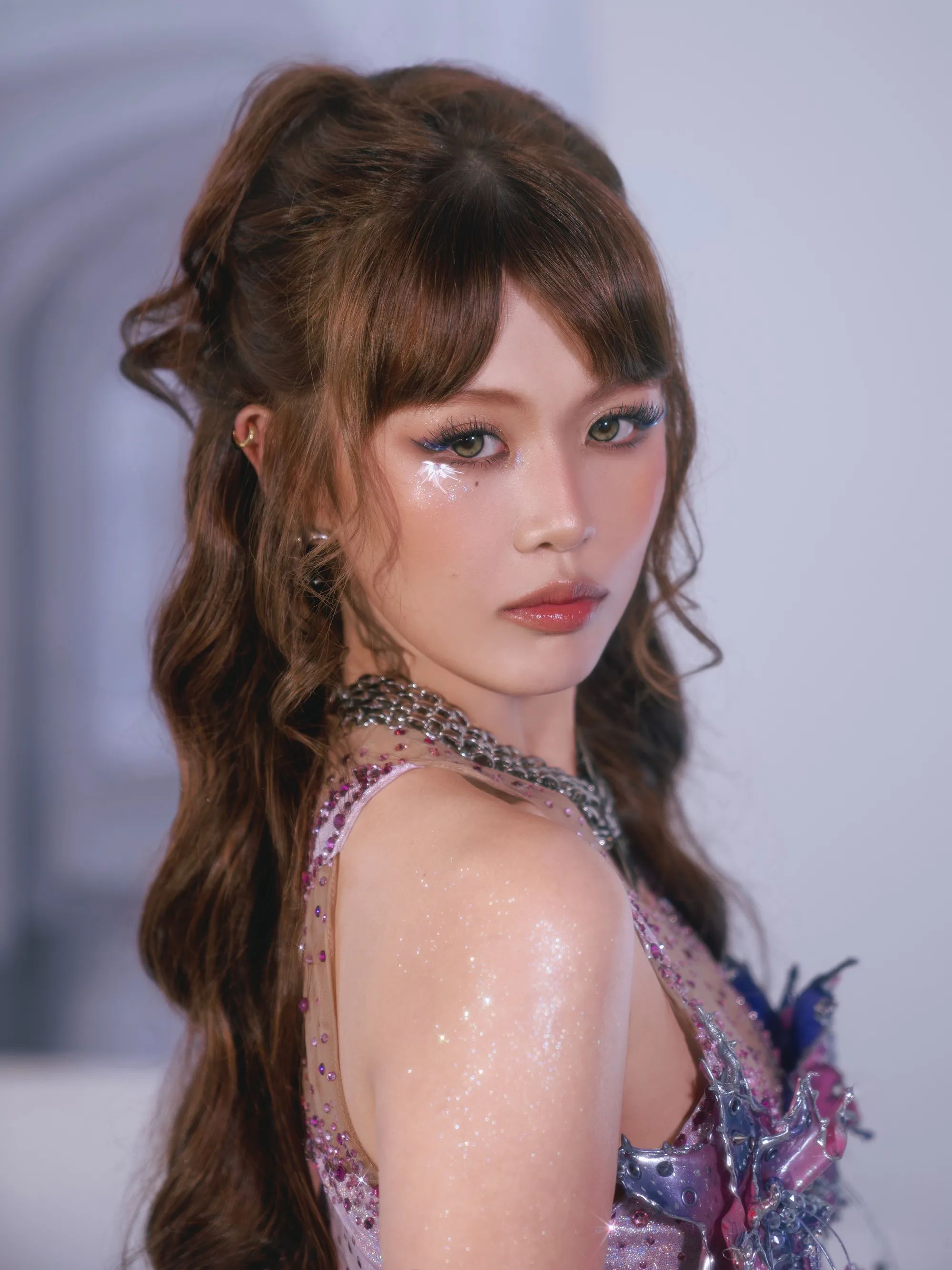 Close-up of a BINI member with bangs and glitter makeup, in a pink metallic look