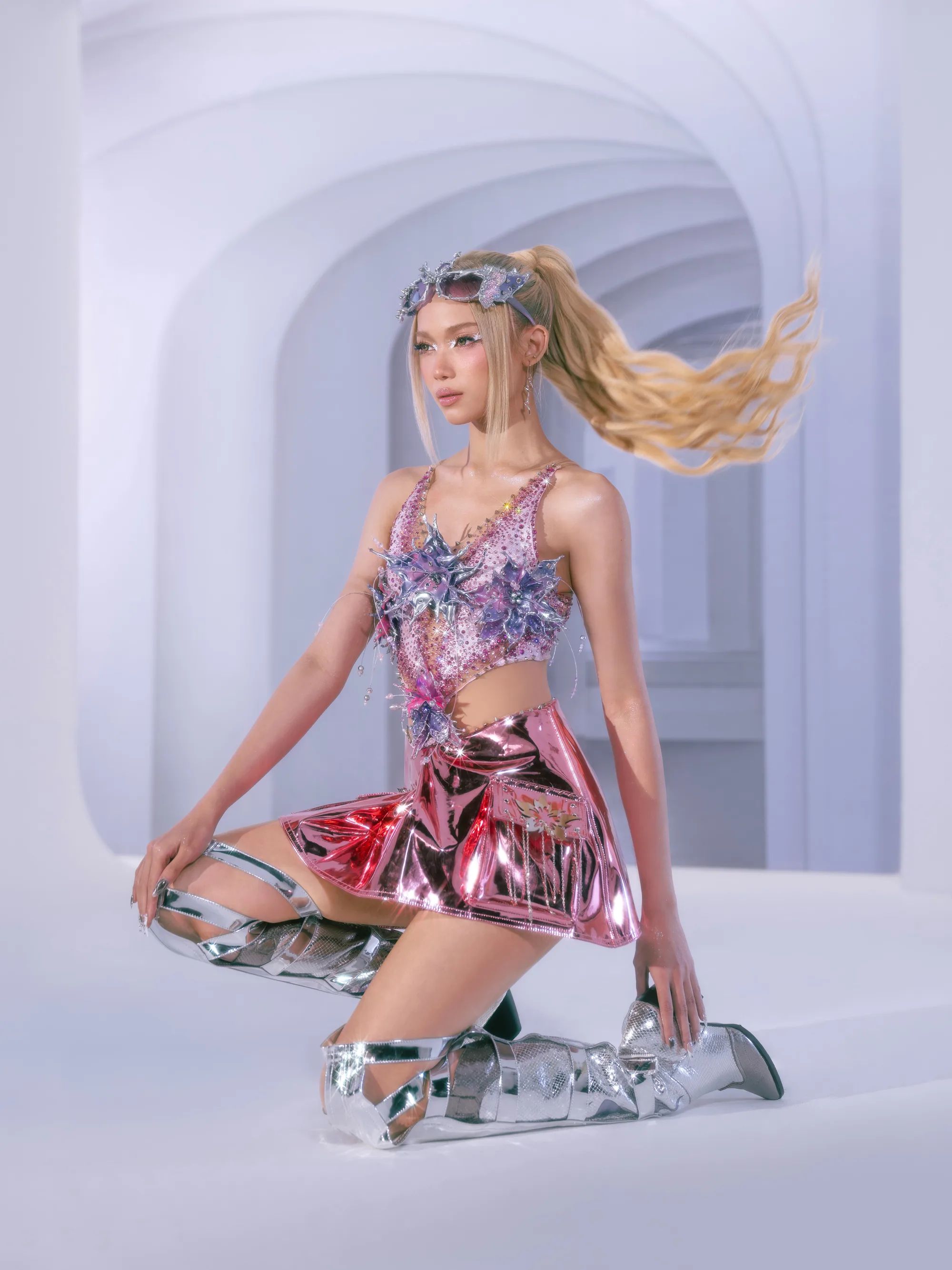 A BINI member with a blonde ponytail in a pink metallic skirt, kneeling, hair swinging